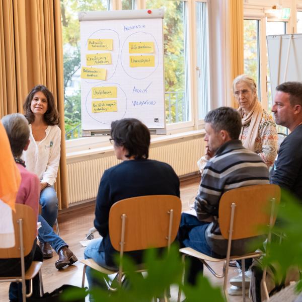 Menschen sitzen im Halbkreis und diskutieren.